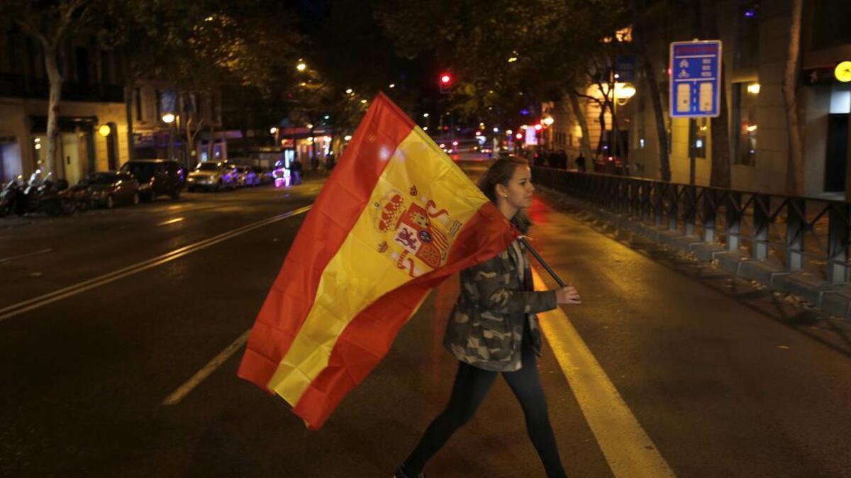 A supporter of the Popular Party carries a Spanish flag as she leaves the party headquarters in Madrid on Sunday. A strong showing Sunday by a pair of upstart parties in Spain's general election upended the country's traditional two-party system, with the ruling Popular Party winning the most votes but falling far short of a parliamentary majority and at risk of being booted from power.