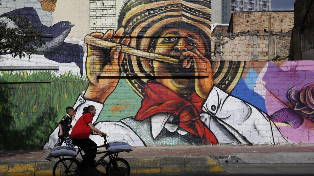 A man cycles past a painting by Colombia’s muralist Bulkar depicting man in traditional clothing from the coast playing the millo flute in Bogota.