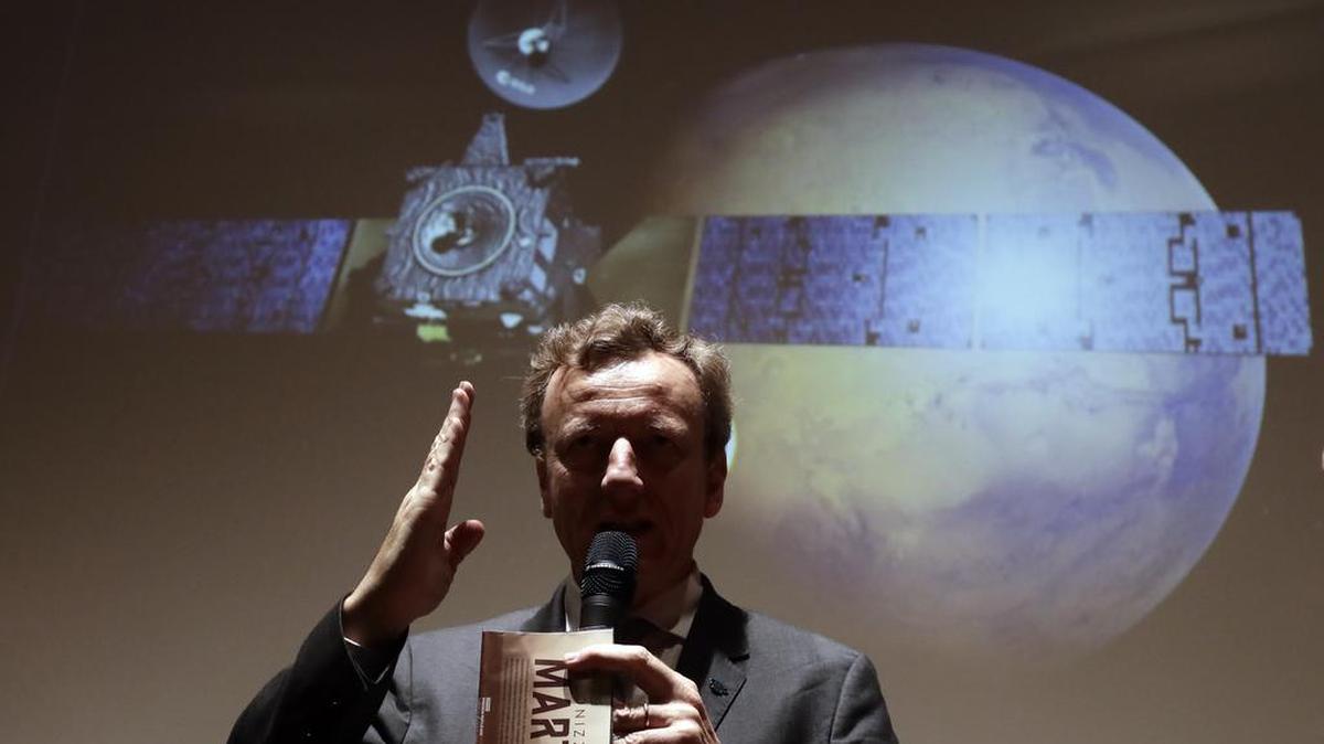 Italian Space Agency President Roberto Battiston talks to journalists in front of a rendering of the Schiaparelli Space Module and of the planet Mars on a movie screen.