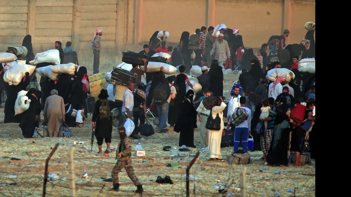 
In this photo taken from the Turkish side of the border between Turkey and Syria, in Akcakale, Sanliurfa province, southeastern Turkey, a masked gunman, believed to be an Islamic State militant runs, as he gives orders to Syrian refugees waiting on the Syrian side of the border in order to cross, to return back to the city of Tal Abyad, Syria, Saturday, June 13, 2015. 

