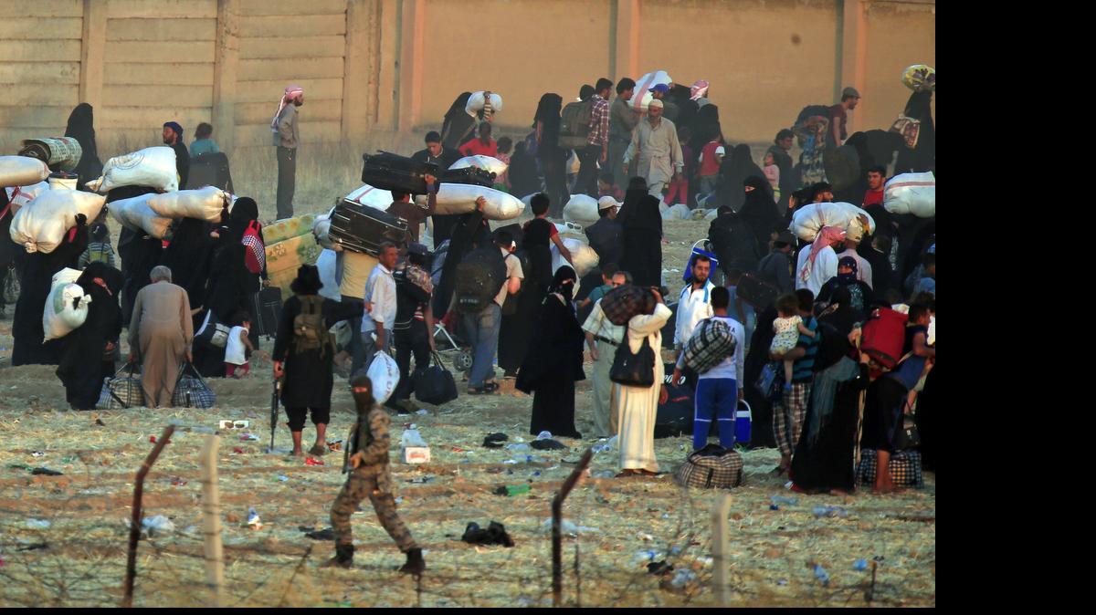 
In this photo taken from the Turkish side of the border between Turkey and Syria, in Akcakale, Sanliurfa province, southeastern Turkey, a masked gunman, believed to be an Islamic State militant runs, as he gives orders to Syrian refugees waiting on the Syrian side of the border in order to cross, to return back to the city of Tal Abyad, Syria, Saturday, June 13, 2015. 
