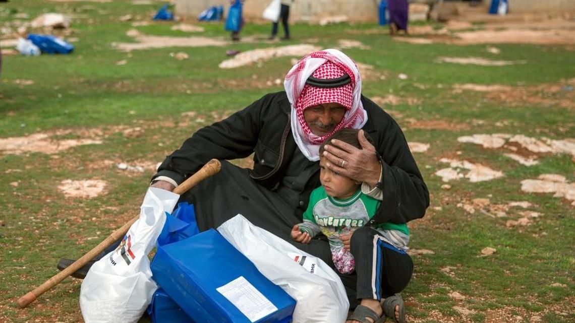 A man and a child sit with an aid package they received from the Russian military near Maarzaf, Syria, on Wednesday. Russian defense ministry spokesman Maj. Gen. Igor Konashenkov said Russia has delivered around 580 tons of food aid to government-held areas since it began airstrikes in support of Syria's government in September 2015. U.S. officials in Washington said a lull in fighting has allowed the delivery of aid to 100,000 people in besieged areas.