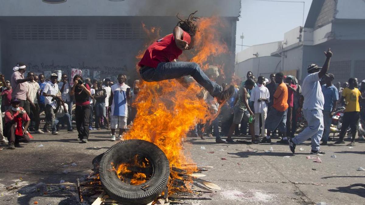 A protester jumps over a burning barricade during protest against President Michel Martelly's government to demand the cancellation of the Jan. 24, elections, in Port-au-Prince, Haiti, Jan. 19, 2016. Disputed election results have brought many broad accusations of electoral fraud from civil society and opposition groups.