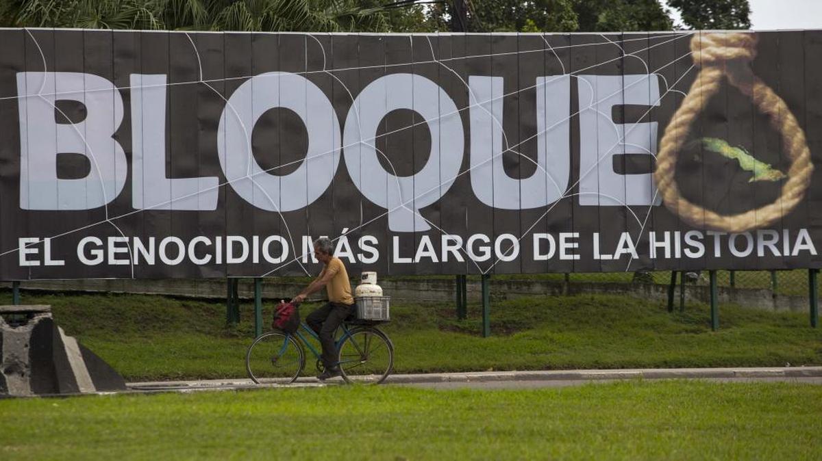 A man carries a gas cylinder on the back of his bicycle as he passes a billboard that reads in Spanish "Blockade: The longest genocide in history" in Havana on Jan. 26, 2016.