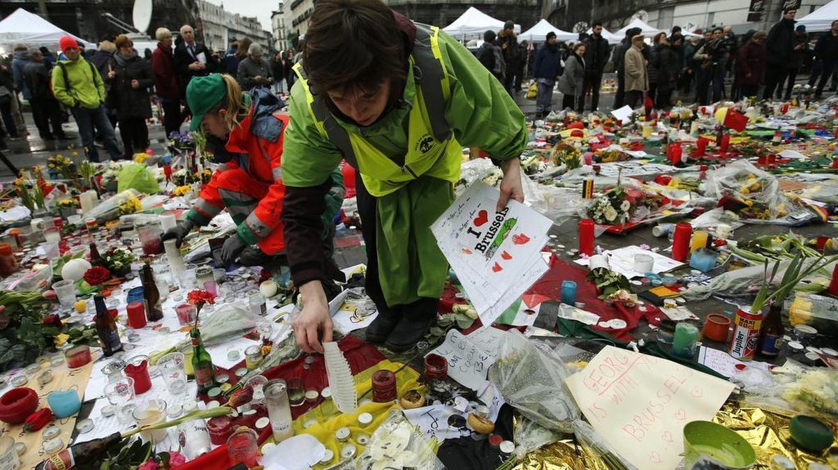 Workers from the City of Brussels collect some of the tributes to preserve them at one of the memorial sites, after the recent attacks in the capital at the Place de la Bourse in Brussels, Friday, March, 25, 2016. Amid signs that life in Brussels was returning to some sort of normality on the third day of mourning the dead, authorities lowered Belgium's terror-threat level by one notch.