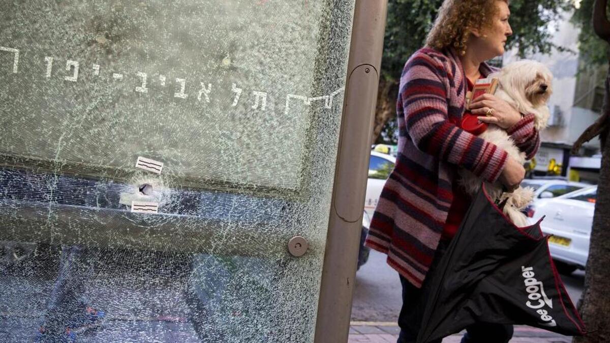 An Israeli woman holds her dog next to a bus station shattered by bullets at the scene of a deadly shooting attack, in Tel Aviv, Israel. For all its years of strife, Israel has rarely seen anything quite like this: an armed, wanted Arab killer on the loose who is spreading fear across the land.