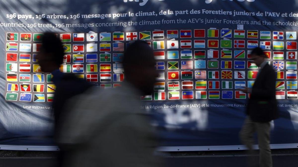 Participants walk by a bannner depicting the flags of 196 countries as part of a project for planting trees from junior foresters and Paris schoolchildren during the COP21, United Nations Climate Change Conference, in Paris, Thursday, Dec. 3, 2015.