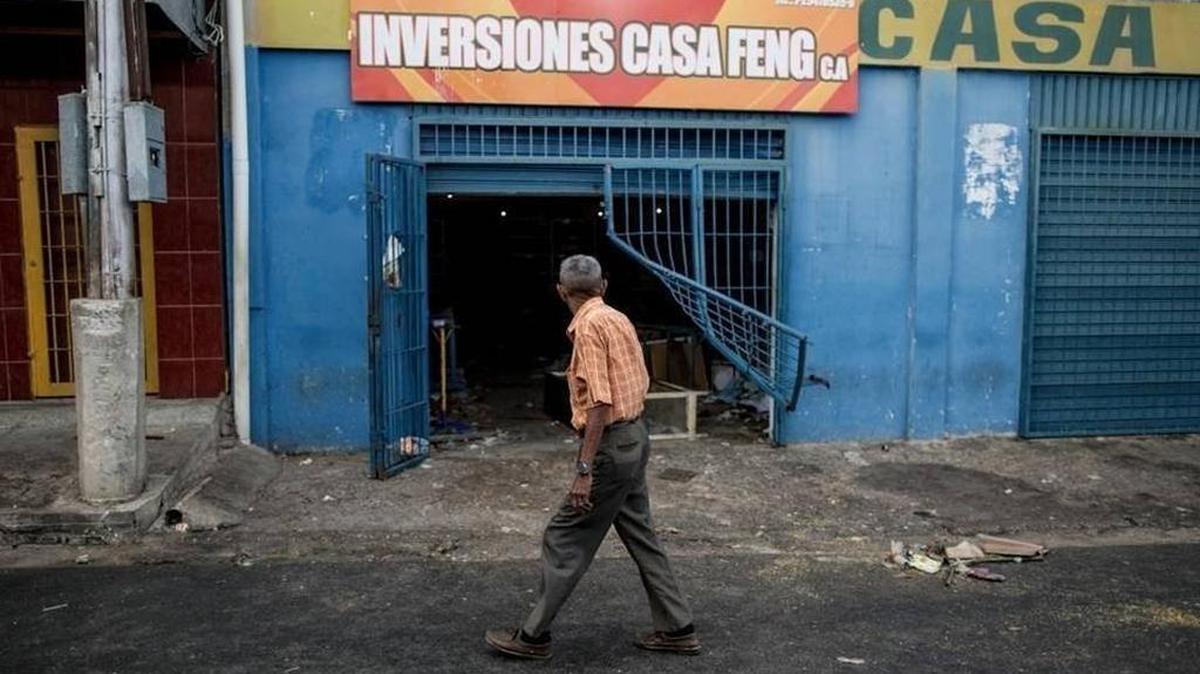 A man walks past a Venezuelan grocery store looted by demonstrators after President Nicolas Maduro threatened to annul 100 bolivar notes.