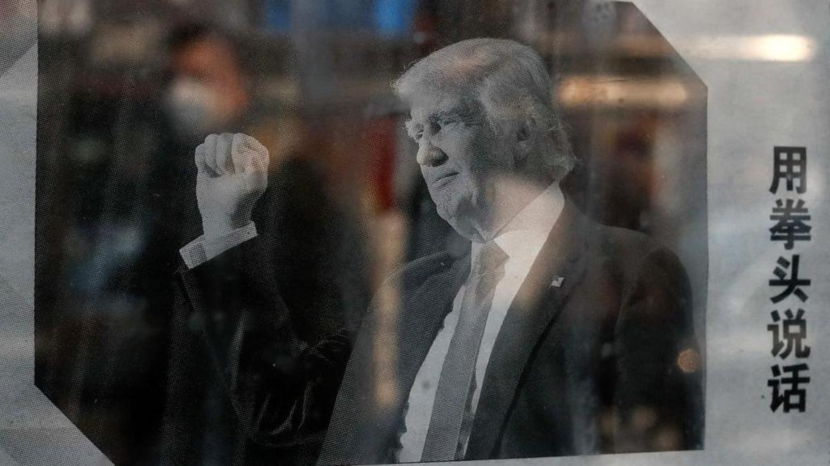 A man with a mask is reflected on a glass-covered bulletin board in Beijing, China, that displays a newspaper article about Donald Trump prior to his inauguration as president. The headline of the article states “Trump uses fist to talk” and reflects Chinese concerns about Trump’s many statements about China, including accusing it of being a currency manipulator.