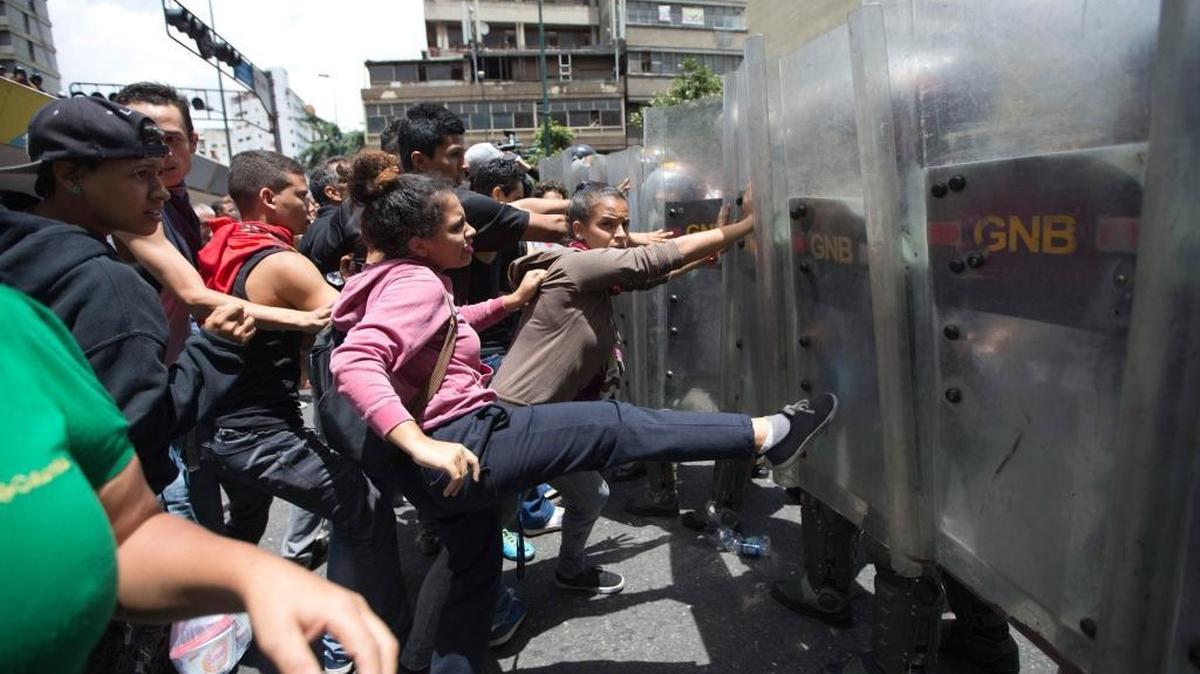Clashes have broken out in Venezuela over shortages of food and other products. In this photo from June 2, a woman kicks the shield of a National Guard soldier during one such incidents a few blocks from the Miraflores presidential palace in Caracas.
