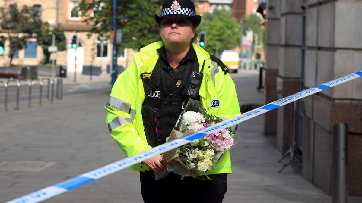 A police officer carries a floral tribute close to the Manchester Arena, the morning after a suicide bomber killed more than a dozen people as an explosion tore through fans leaving a pop concert in Manchester, England, Tuesday, May 23, 2017.