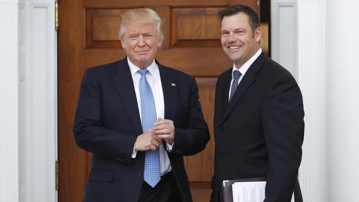 Kansas Secretary of State Kris Kobach, right, holds a stack of papers as he meets with then President-elect Donald Trump.