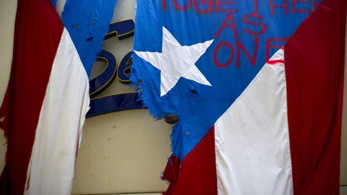 A damaged Puerto Rican national flag spray painted with the words "Together as One" hangs from the facade of a business, in San Juan, Puerto Rico.
