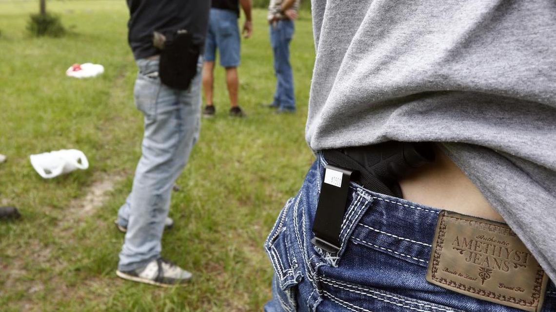 Crestview Baptist Church member Courtney Davis shows where she holsters her concealed firearm while another participant uses a hip holster as they await their turn to shoot during the live fire portion of a enhanced concealed carry class sponsored by the church for members and area residents in Petal, Miss.