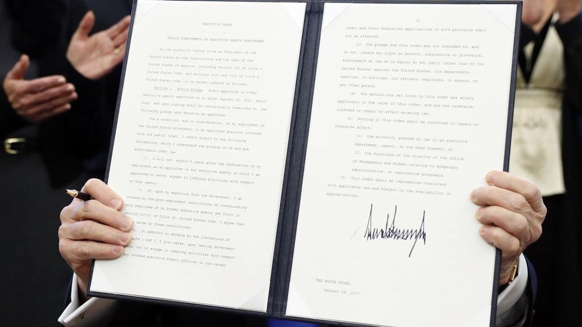 President Donald Trump holds up a signed Executive Order in the Oval Office of the White House, Saturday, Jan. 28, 2017 in Washington. The document includes restrictions against lobbying for "Every appointee in every executive agency appointed on or after January 20, 2017..."