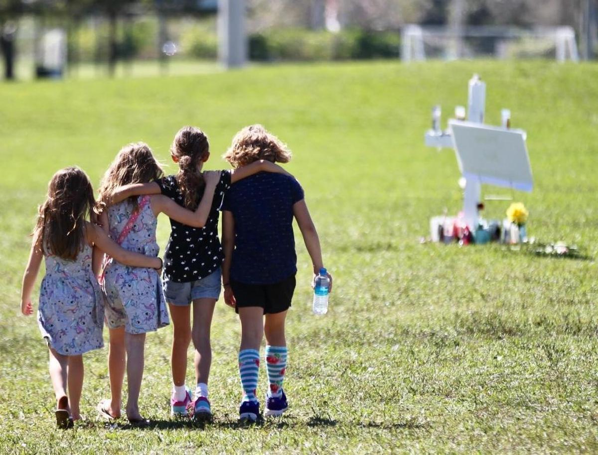 Four children with hands around each other approach a vigil post at Park Trails Park in Parkland honoring the 17 students that were shot at the high school.