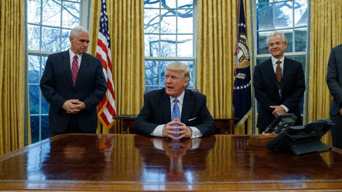 Vice President Mike Pence, left, and National Trade Council adviser Peter Navarro, right, wait for President Donald Trump to sign three executive orders in the Oval Office.
