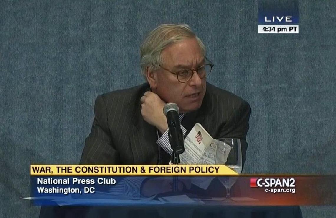 Harvey Rishikof holding a copy of the Constitution as he moderated a Sept. 16, 2014 debate between attorneys John Yoo and Bruce Fein.