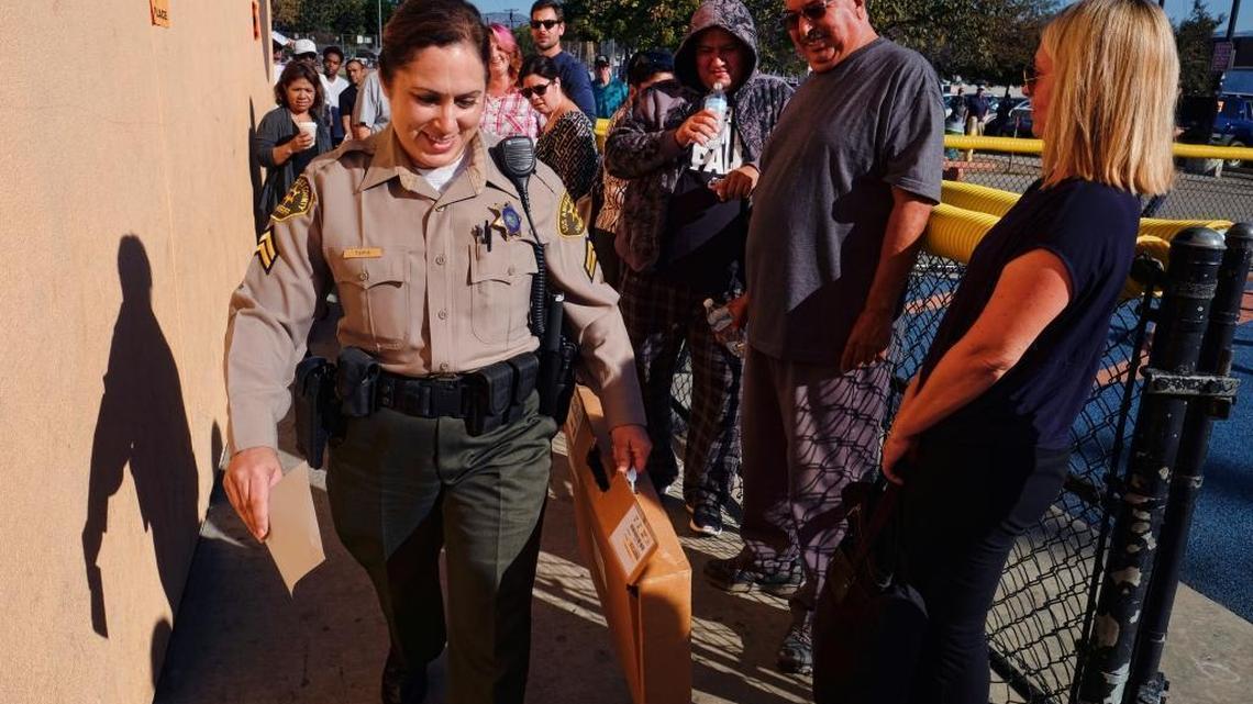 Voters who had waited hours in line to vote watch as a Los Angeles County sheriff's deputy arrives with ballot marking devices in the Van Nuys section of Los Angeles on Tuesday, Nov. 8, 2016. Frustrations ran high at the Los Angeles polling place as voters were left waiting when ballot marking devices arrived late.