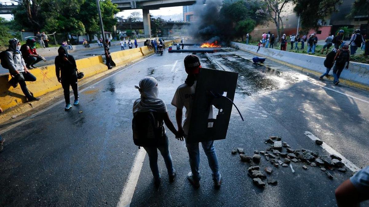 A couple holds hands at a road block set by anti-government protesters in Caracas, Venezuela. Protesters shut down the capital city's main highway to express their disgust with the administration of President Nicolas Maduro.