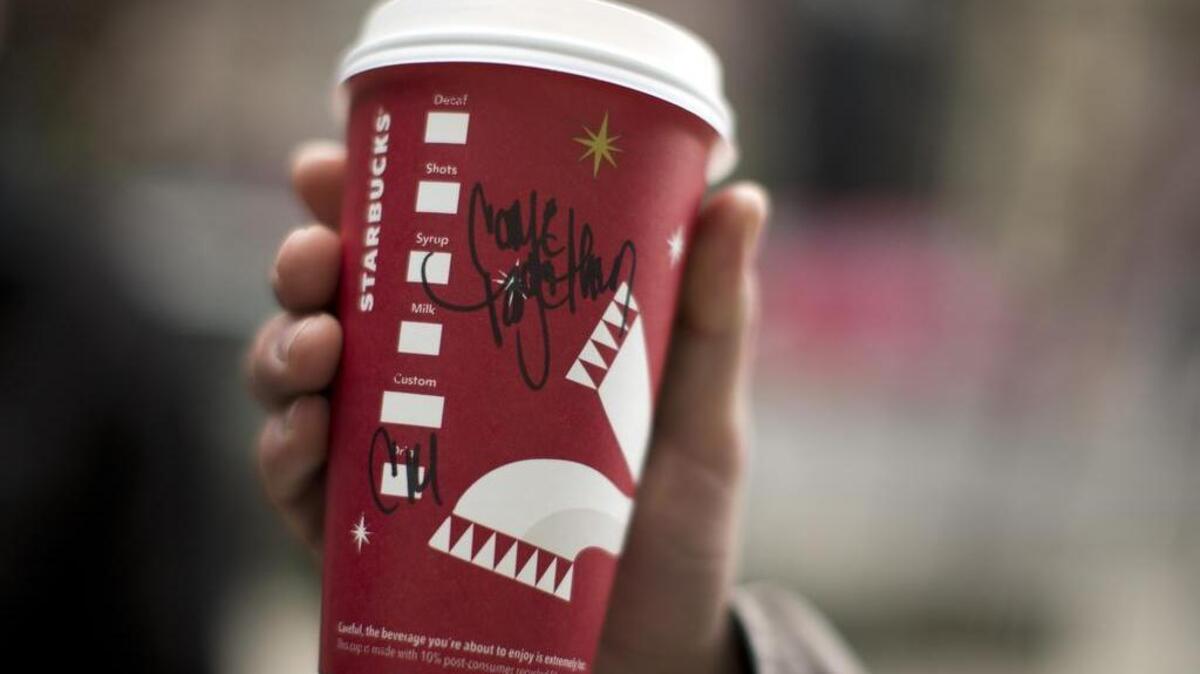 Justin McCartney of Hampton, Va., holds up a cup with the words "Come Together" written on it outside a Starbucks cafe in Washington, Thursday, Dec. 27, 2012. Starbucks is using its coffee cups to jump into the political fray in Washington. The world's biggest coffee chain is asking employees at cafes in the Washington area to scribble the words "Come Together" on cups for drink orders on Thursday and Friday. CEO Howard Schultz says the words are intended as a message to lawmakers about the damage being caused by the divisive negotiations over the "fiscal cliff."