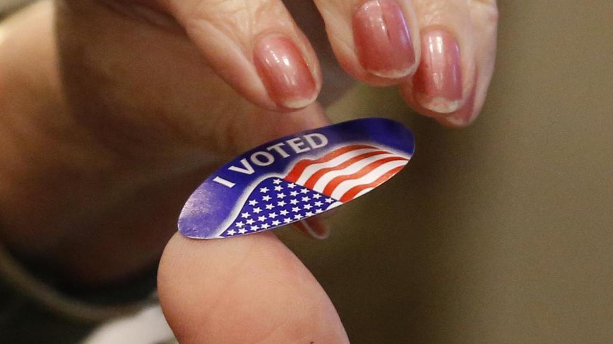 A voter, top, picks up a "I Voted" sticker from Ridgeland, Miss., poll worker, Cliff Smith after voting Tuesday, Nov. 8, 2016.