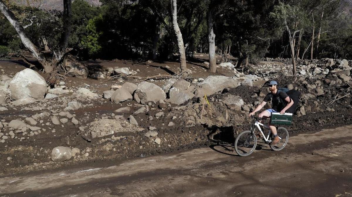 A man rides a bicycle down a road damaged from storms in Montecito, Calif. in January.
