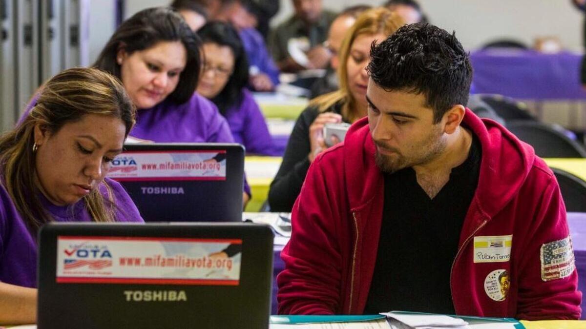 In this March 31, 2014, file photo, SEIU-UHW worker Kathy Santana, left, assists Ruben Torres, 27, during a health care enrollment event at the SEIU-UHW office in Commerce, Calif.