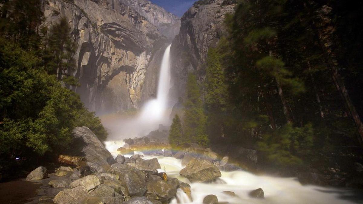 A faint moonbow forms in the mist below Lower Yosemite Falls as seen in this 30-second exposure in Yosemite National Park.