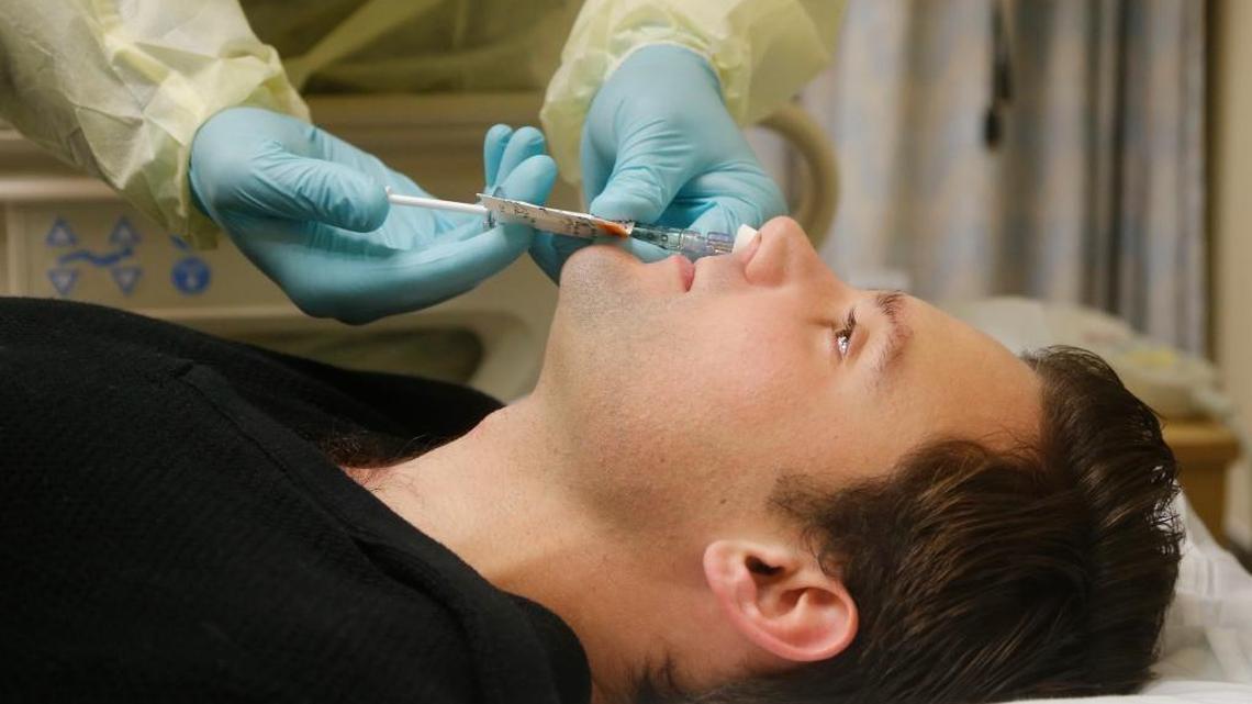 In this Jan. 14, 2014, photo, Daniel Bennett, 26, of College Park, Md., has live flu virus sprayed into his nose as part of a study at the National Institutes of Health in Bethesda, Md.
