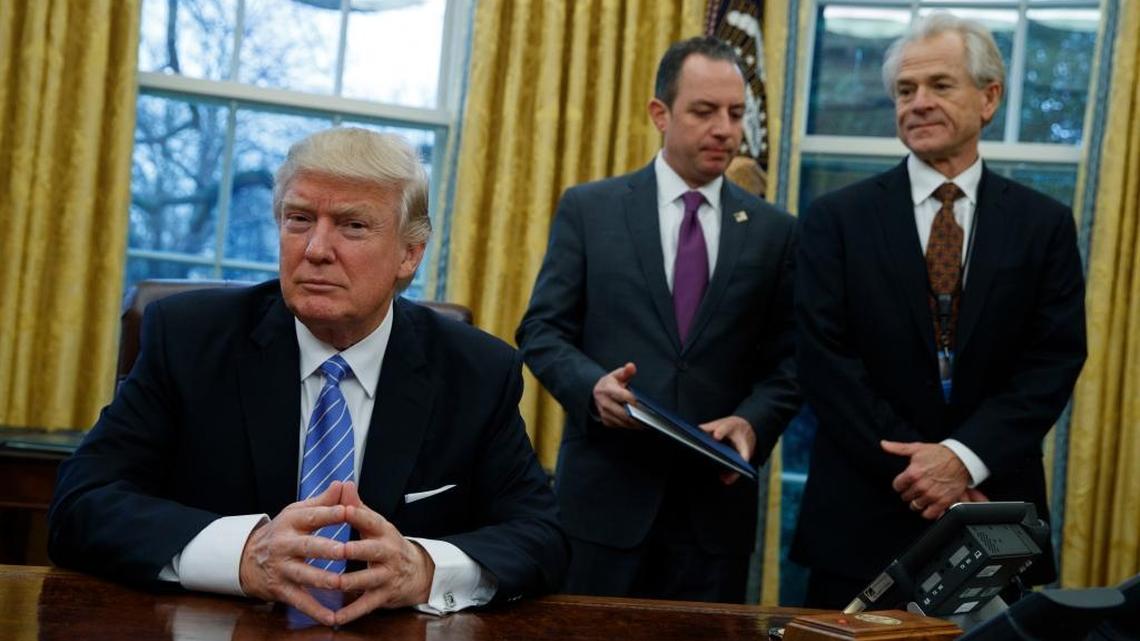 National Trade Council adviser Peter Navarro, far right, and White House Chief of Staff Reince Priebus, center, await President Donald Trump's signing of three executive orders, Jan. 23, 2017, in the Oval Office of the White House in Washington.