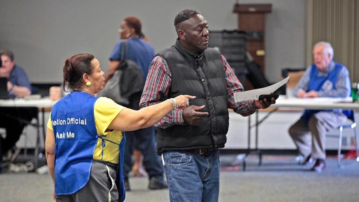 A poll worker at the Durham Main Library directs a voter with his ballot to an open voting space during early afternoon voting the Durham County Main Library precinct Tuesday, March 15, 2016.