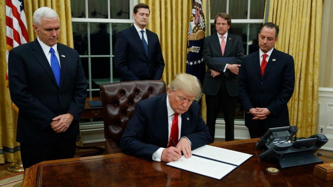 President Donald Trump, flanked by Vice President Mike Pence and Chief of Staff Reince Priebus, signs his first executive order on health care, Friday, Jan, 20, 2017, in the Oval Office of the White House in Washington.