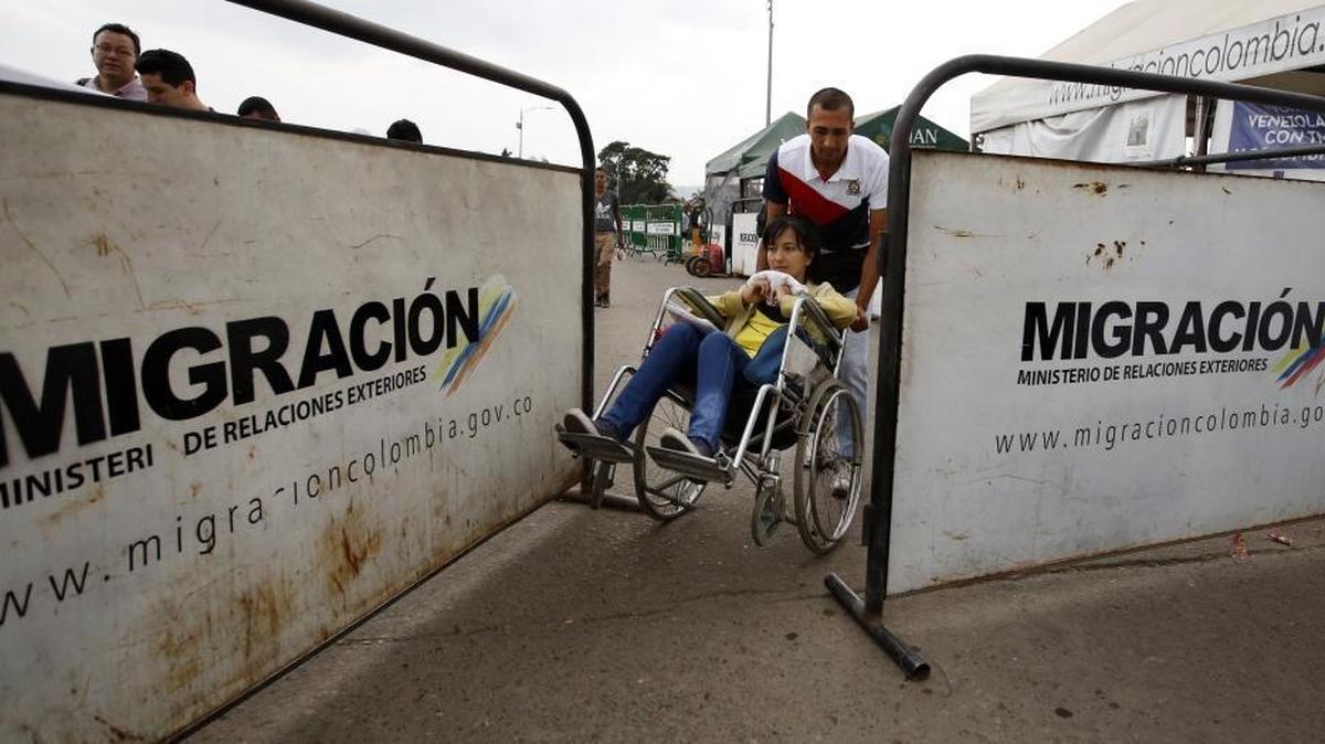 In this Feb. 22, 2018 photo, Venezuelan Nelson Gonzalez pushes his wife Grecia Sabala in a wheelchair across the international border back into Venezuela. Sabala returned after receiving permission to receive chemotherapy treatment in Cucuta, on the Colombian side of the border. Venezuela's health crisis is spilling into neighboring Colombia as thousands of migrants arrive in need of urgent medical attention.