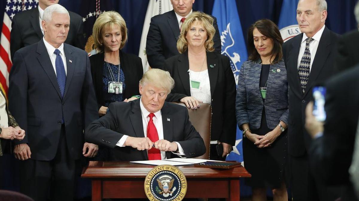 President Donald Trump takes the cap off a pen before signing executive order for immigration actions to build border wall as Vice President Mike Pence, left, and Homeland Security Secretary John F. Kelly, right, and others watch during Trump's a visit to the Homeland Security Department headquarters in Washington, Wednesday, Jan. 25, 2017.