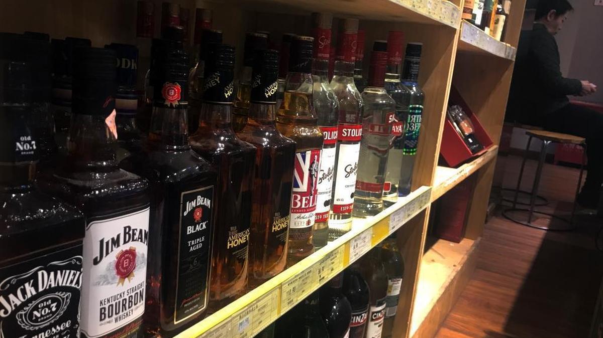 A worker sits near a shelve displaying bottles of American whiskey for sale at a supermarket in Beijing Wednesday.