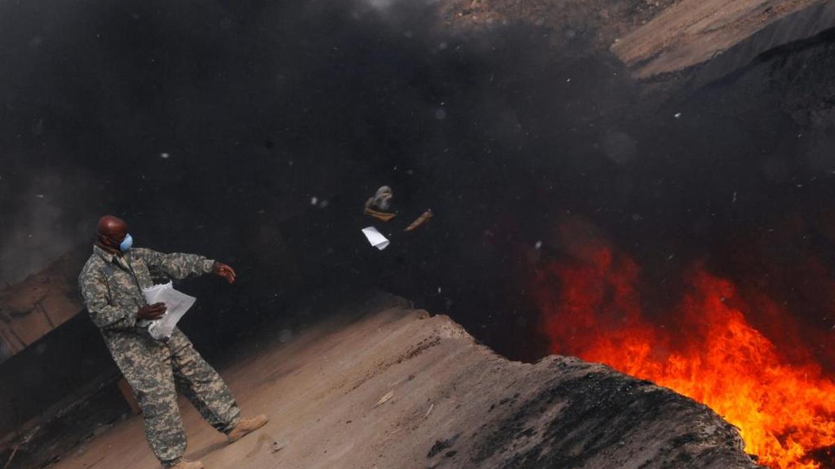 U.S. Air Force Master Sgt. Darryl Sterling tosses unserviceable uniform items into a burn pit at Balad Air Base, Iraq, on March 10, 2008. The noxious smoke plumes that wafted over the military base have given rise to health concerns.