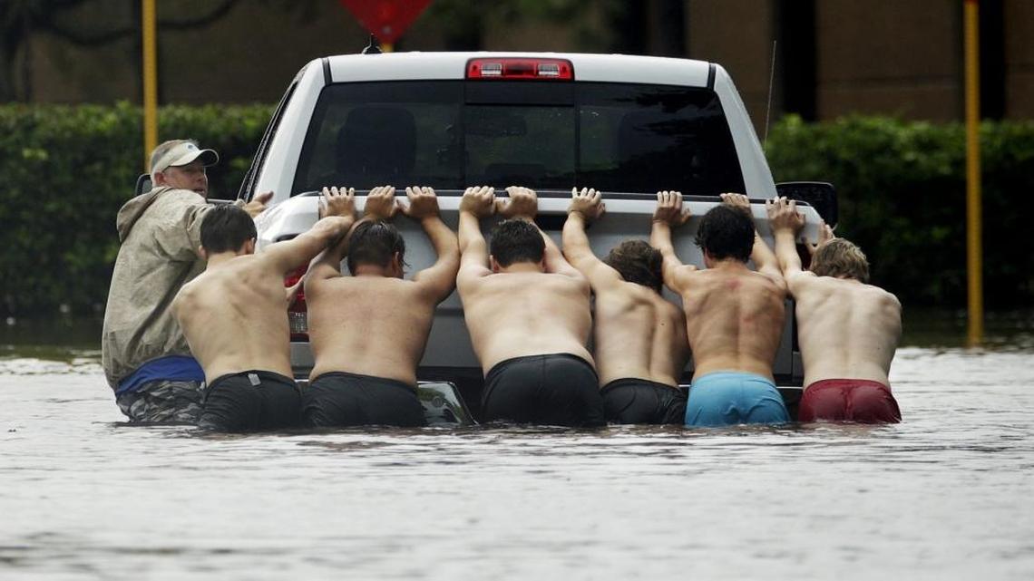 Men team up to push a stalled pickup truck through a flooded street in Houston.