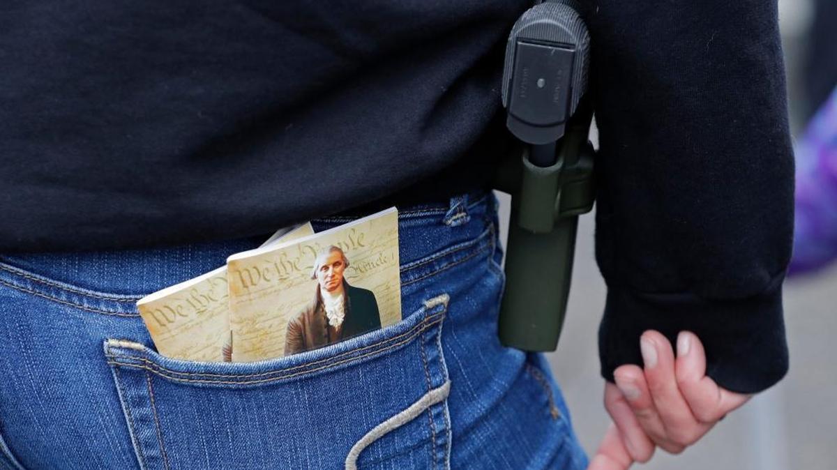 In this Jan. 12, 2018 photo, a woman wears a gun in a holster next to two copies of the U.S. Constitution during a gun rights rally at the Capitol in Olympia, Wash. A Washington state Legislature Senate committee held a public hearing Monday, Jan. 15, on several bills related to guns, including measures to prohibit high-capacity magazines and to ban so-called bump stocks, trigger modification devices designed to increase the rate of fire of a firearm.