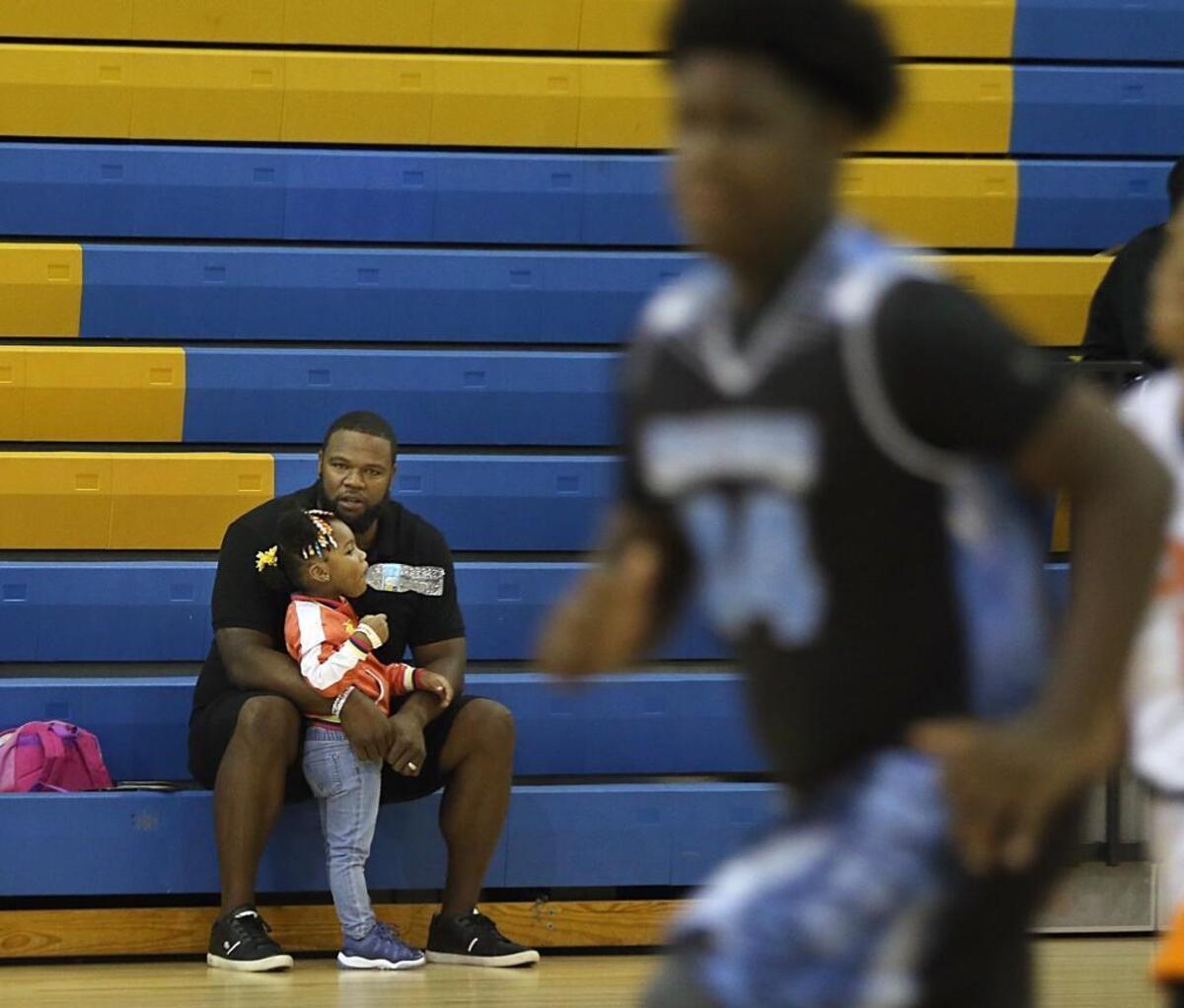 Former Miami Dolphin Vernon Carey with his 2-year-old daughter Dynver watching as his 11-year-old son, Jalen, with the Broward Sharks, plays a state championship youth basketball game at Cypress Bay High School in Weston on Friday, June 09, 2017.