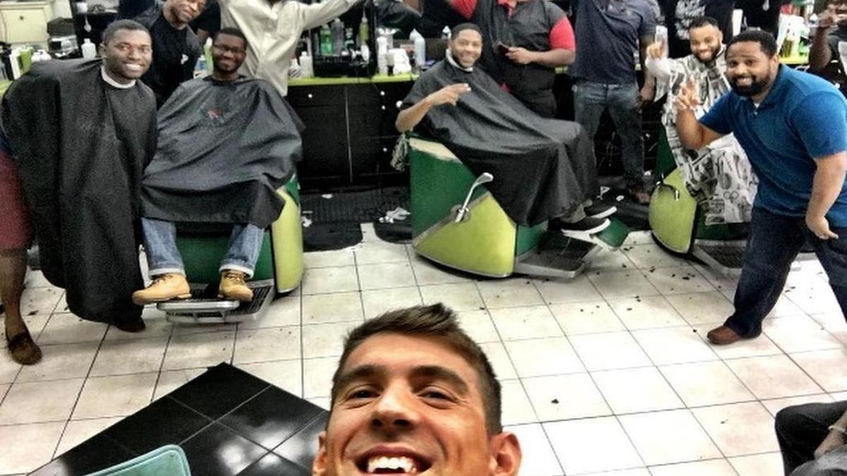 Michael Phelps takes a photo with smiling barbers and customers after getting a haircut at Vintage the Barber Shop in Atlanta on his way to the Olympics.