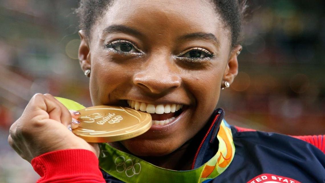 United States' Simone Biles bites her gold medal for the artistic gymnastics women's individual all-around final at the 2016 Summer Olympics in Rio de Janeiro, Brazil, Thurs., Aug. 11, 2016.
