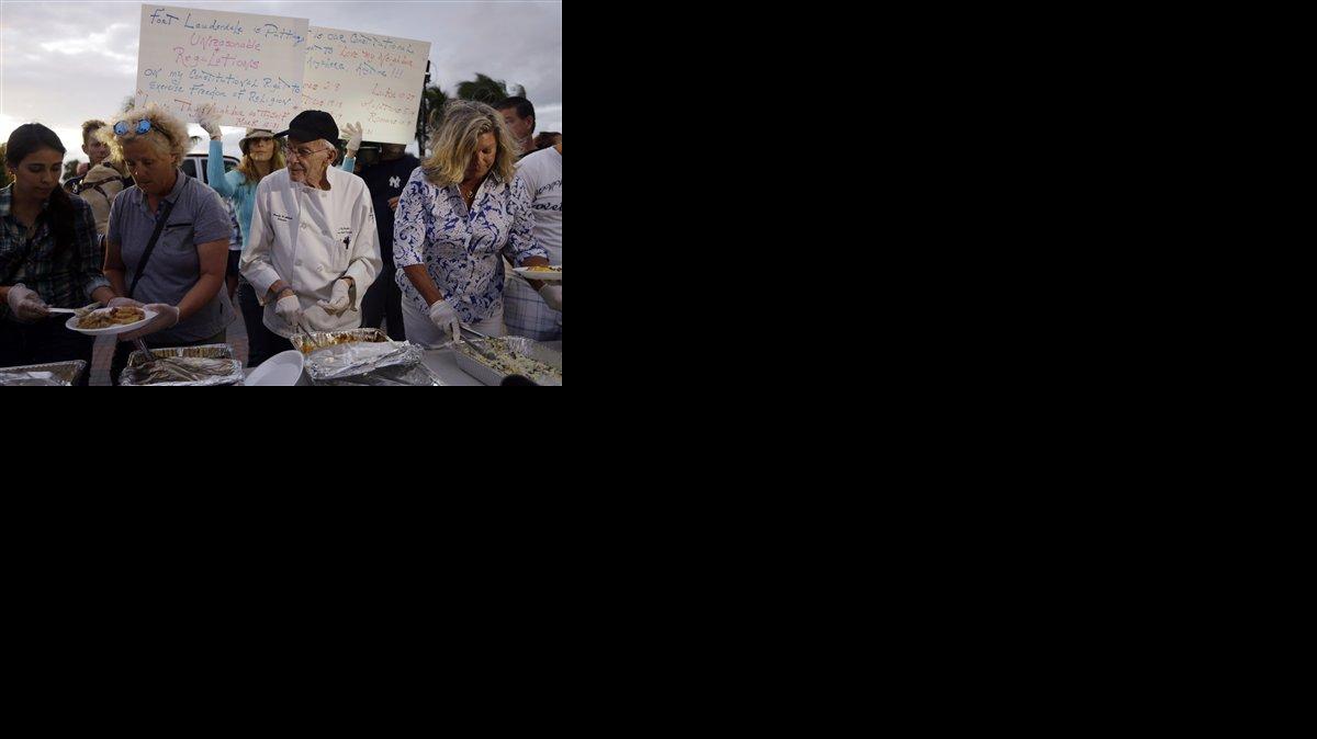 El defensor de los desamparados Arnold Abbott, de 90 años, director del grupo sin fines de lucro Love Thy Neighbor Inc., al centro, sirve comida a desamparados con ayuda de voluntarios en un estacionamiento público junto a una playa, el miércoles, 5 de noviembre del 2014, en Florida.